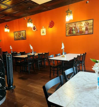 Warm orange dining room with tables, chairs and pendant lights at Lutf Indo-Pak Cuisine
