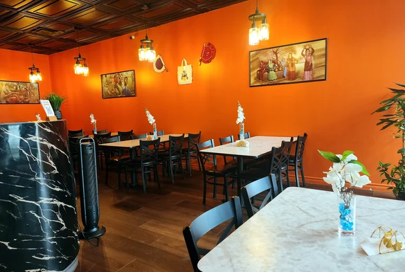 Warm orange dining room with tables, chairs and pendant lights at Lutf Indo-Pak Cuisine